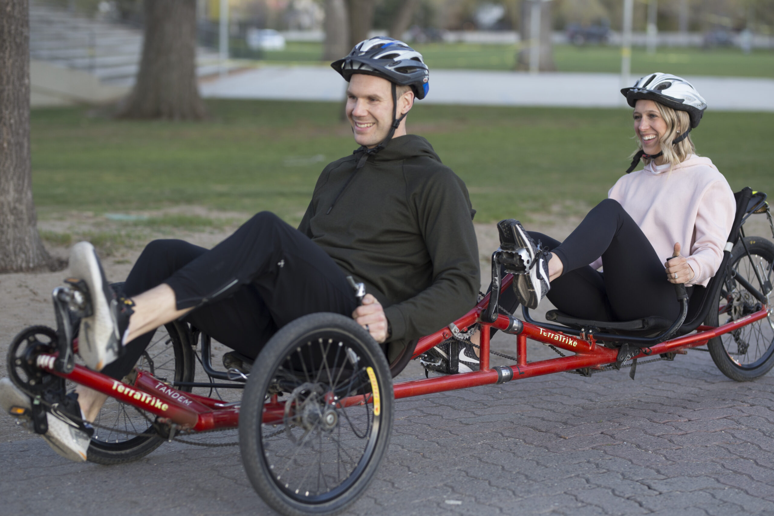 A man (in front) and a woman (behind) riding a red tandem recumbent cycle