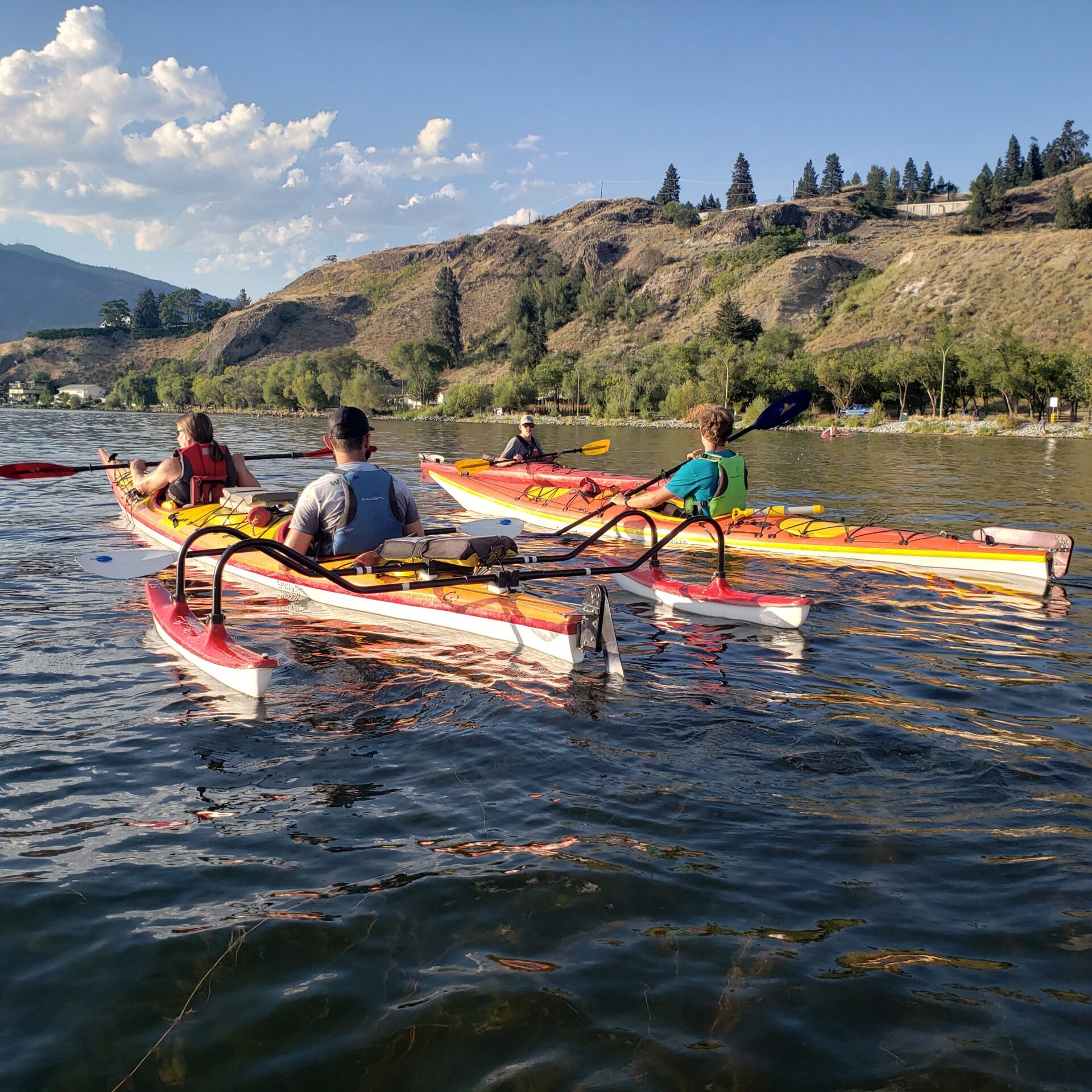 Two orange and yellow kayaks. One is a tandem kayak with two pontoons on the back. The picture is taken from behind so the user's faces are not visible.