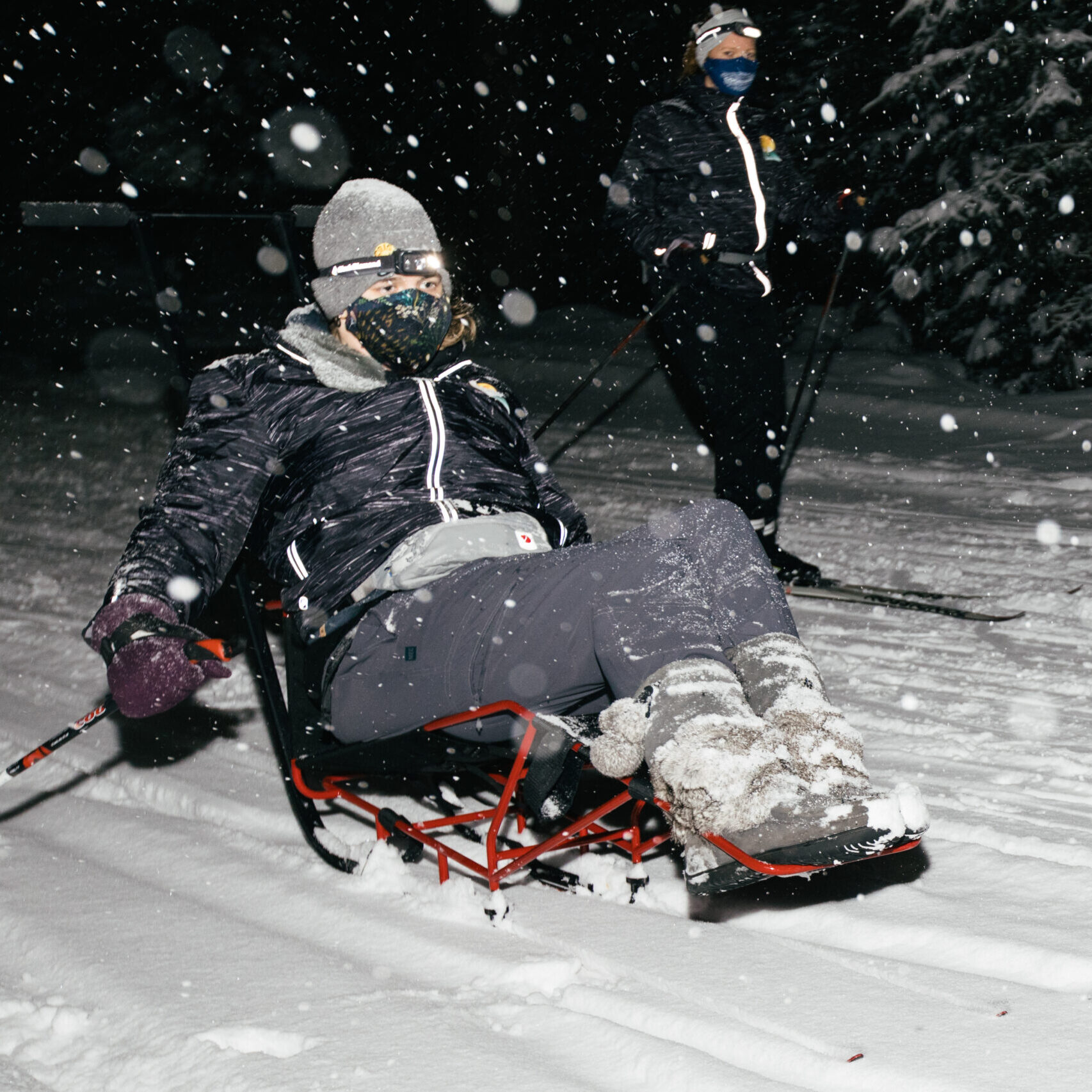 A woman using s nordic sit-ski at night during a snowstorm at night.