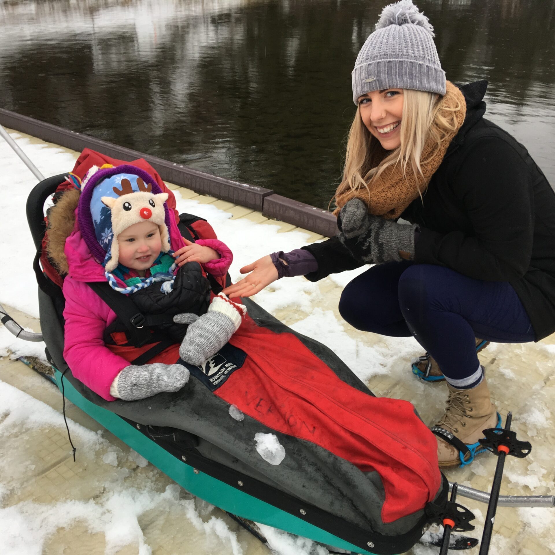 a young girl in a sled. a woman is kneeling beside her.